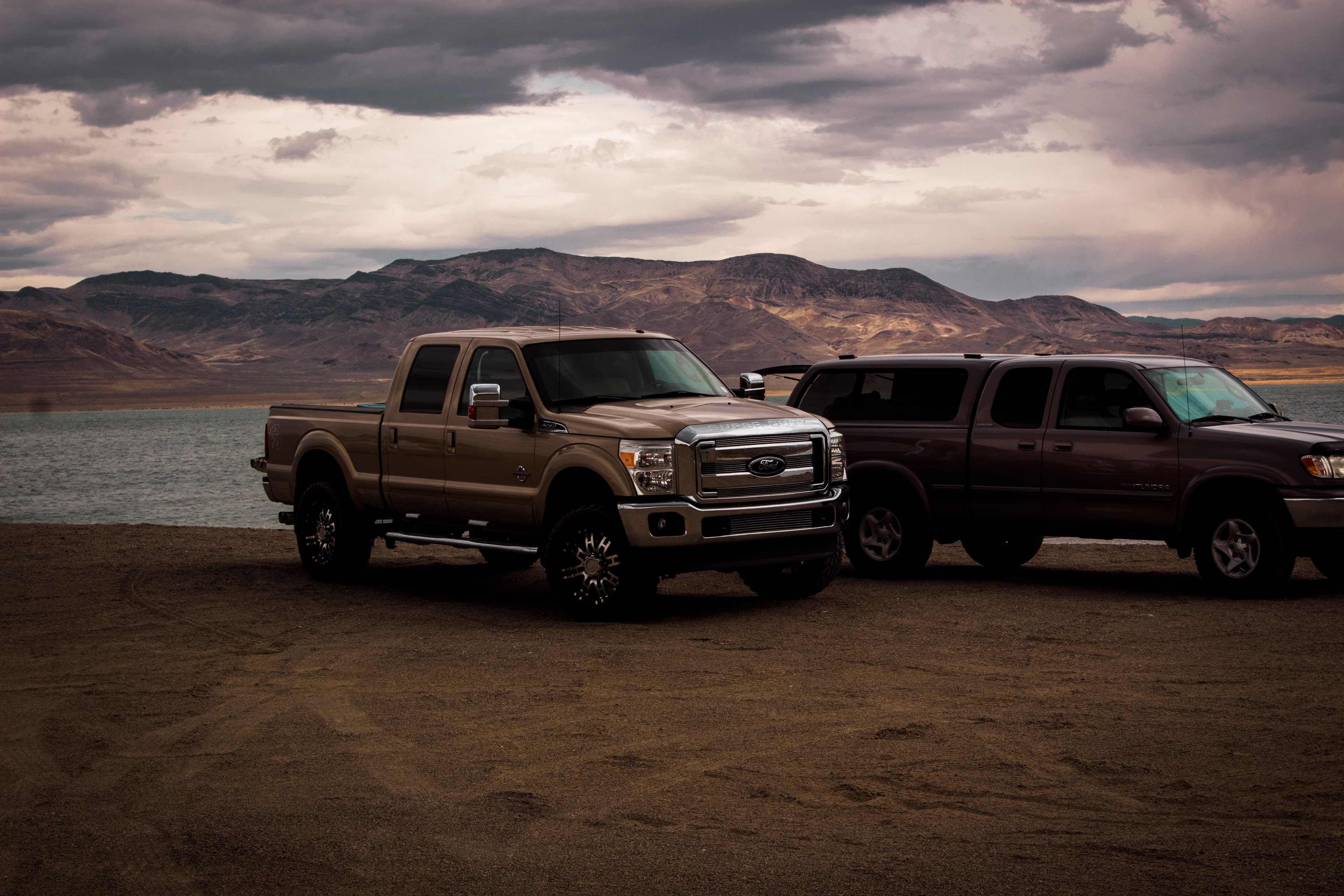 Two pickup trucks parked on a lakeshore